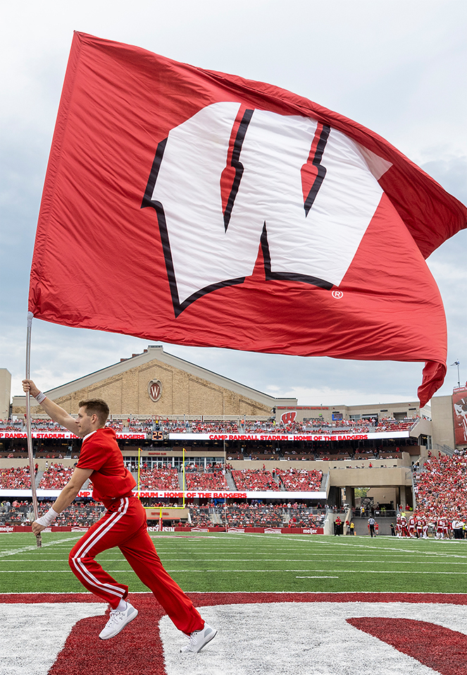 A person running a Wisconsin flag along the endzone at Camp Randall Stadium