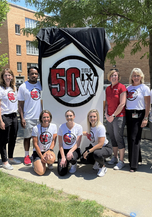 A group standing in front of a sign for the 50th anniversary of Title IX